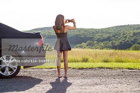 Young woman photographing rural scene with camera phone