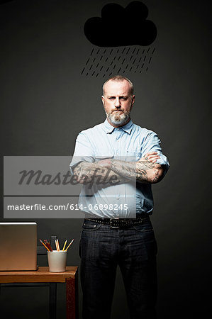 Man with arms crossed standing under dark rain cloud