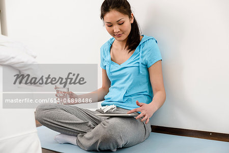Woman sitting cross-legged on mat using digital tablet
