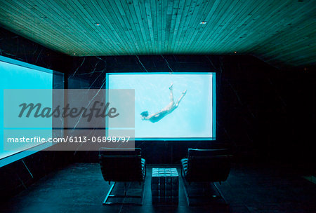 View of woman swimming underwater from window in pool room