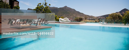 Woman sunbathing on lounge chair next to luxury swimming pool with mountain view