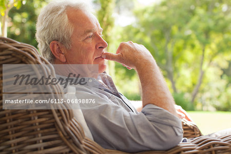 Pensive senior man sitting in wicker armchair on porch