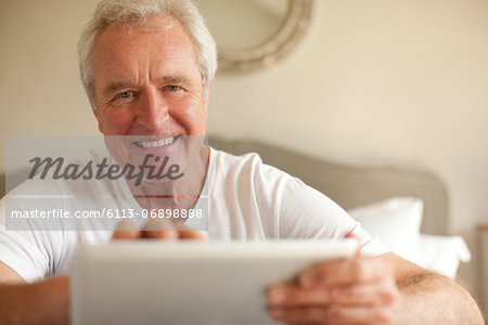 Portrait of smiling senior man using digital tablet in bedroom