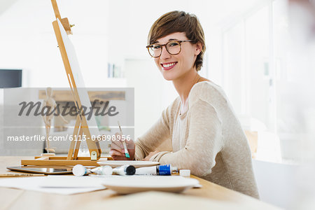 Portrait of smiling woman painting at easel on table