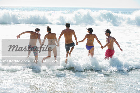 Friends holding hands and splashing in ocean