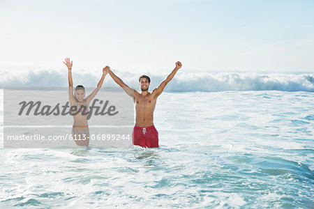 Portrait of enthusiastic couple holding hands with arms raised in ocean