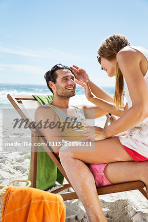 Woman applying sunscreen to man's nose at beach