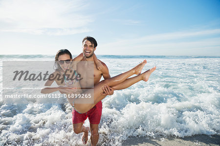 Enthusiastic man carrying woman on beach