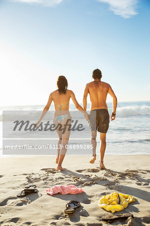 Couple holding hands and walking toward ocean on beach