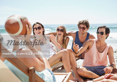 Happy friends with football hanging out at beach