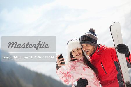 Happy couple with skis taking self-portrait with camera phone