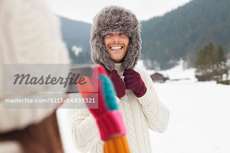 Woman photographing man wearing fur hat in snowy field