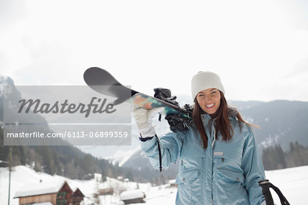 Portrait of enthusiastic woman carrying skis in snowy field