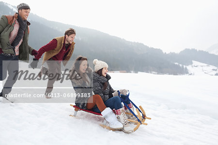 Enthusiastic friends sledding in snowy field