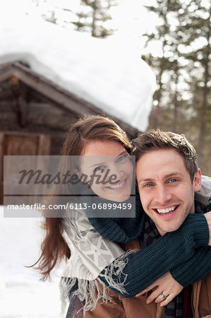 Portrait of happy couple hugging in snow outside cabin