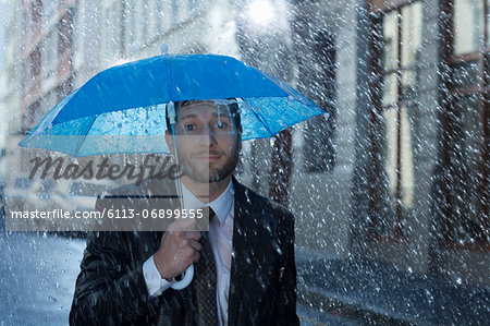 Portrait of businessman with tiny umbrella in rain