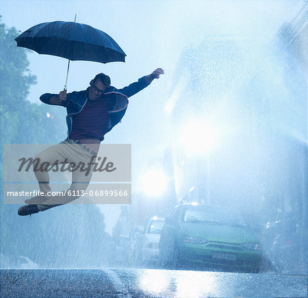 Enthusiastic man with umbrella jumping in rain