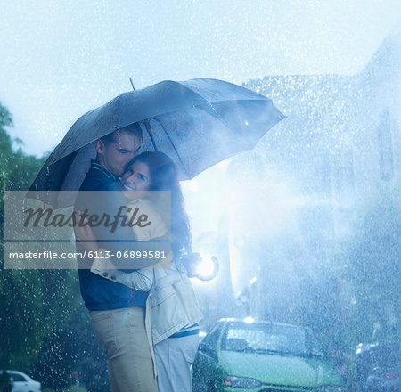 Happy couple hugging under umbrella in rain