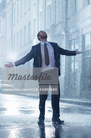 Businessman standing with arms outstretched in rainy street