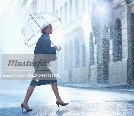 Happy businesswoman with umbrella walking across rainy street