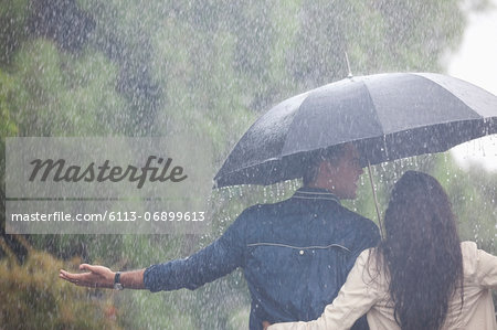 Couple walking with arms outstretched under umbrella in rain