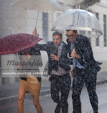Happy business people with umbrellas running in rainy street