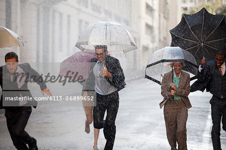 Enthusiastic business people with umbrellas running in rainy street