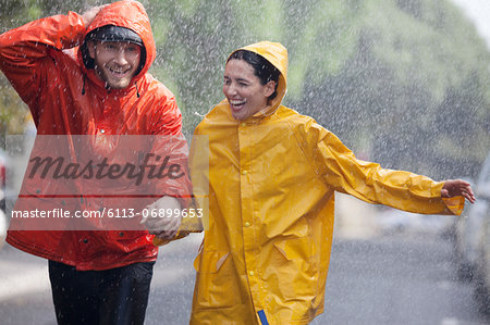 Happy couple holding hands and running in rainy street