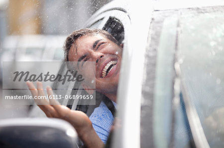 Enthusiastic man in car looking out window at rain