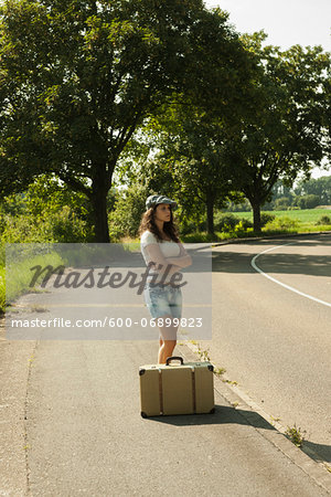 Teenaged girl standing on the side of the road with suitcase, in summer, Germany