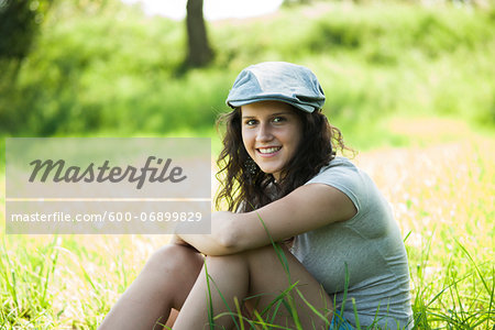 Portrait of teenaged girl sitting in field, smiling and looking at camera, Germany