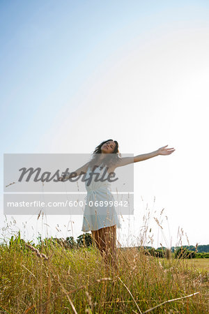 Teenaged girl standing in field with arms outstretched, Germany
