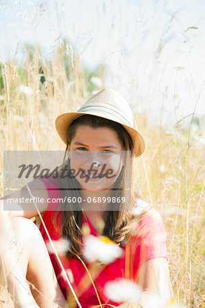 Portrait of Girl wearing hat, sitting in field and smiling at camera, Germany