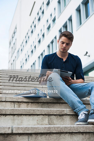 Young man sitting on steps outdoors, using tablet computer, Germany