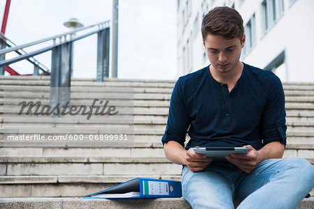 Young man sitting on steps outdoors, using tablet computer, Germany