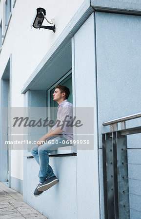 Young man sitting on ledge outdoors, Germany