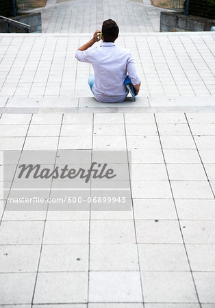 Backview of young man sitting on steps outdoors, using cell phone, Germany