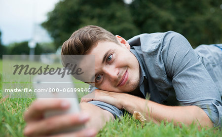 Close-up of young man lying on grass, looking at cell phone, Germany Close-up of young man lying on grass, looking at cell phone, Germany