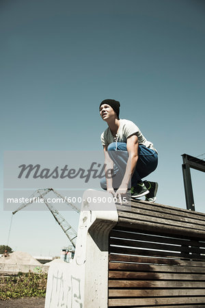 Teenager crouching down on barrier, anticipating next move, freerunning, Germany