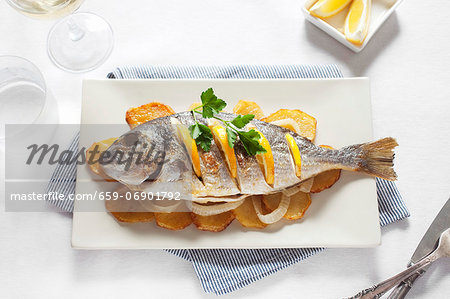 Grilled gilt-head bream with oranges on top of potato slices