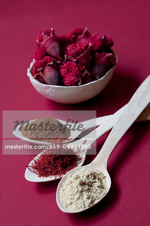 Spoons of liquorice root powder, saffron threads and cinnamon, with a bowl of pomegranate flowers