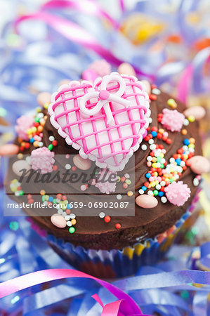 A chocolate cupcake topped with a pink heart for a party