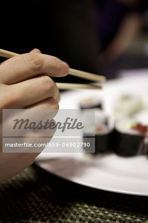 A hand reaching for a piece of sushi using chopsticks