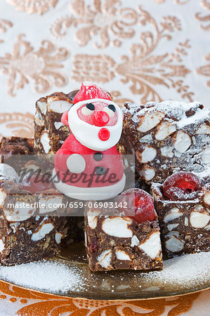 a model in red marzipan of father Christmas standing on squares of rocky -road cakes for Christmas with gold patterened paper