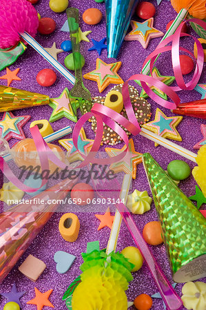 overview still life of various party decorations, party poppers sweets and straws for the party table on a purple glittery table