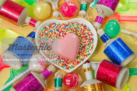 overview still life close up of heart dish with a pink chocolate heart shape and coloured party poppers and plastic ice cream spoons