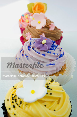 close up, selective focus of a row of coloured cup cakes, decorated with orange, pink and purple flowers on top
