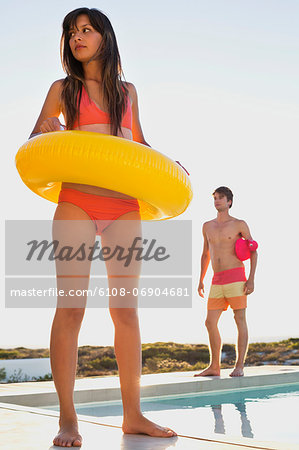 Woman walking with inflatable ring at the poolside with a man behind her