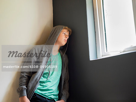 Teenage boy leaning against a wall and thinking