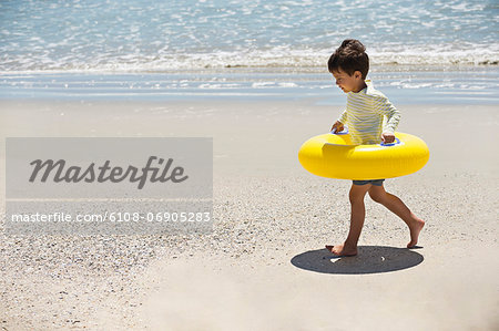 Boy holding an inflatable ring and walking on the beach